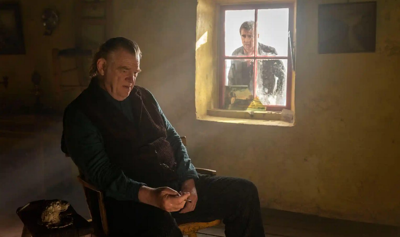 The Banshees of Inisherin: Pádraic (Colin Farrell) buscando a través de la ventana a Colm (Brendan Gleeson).